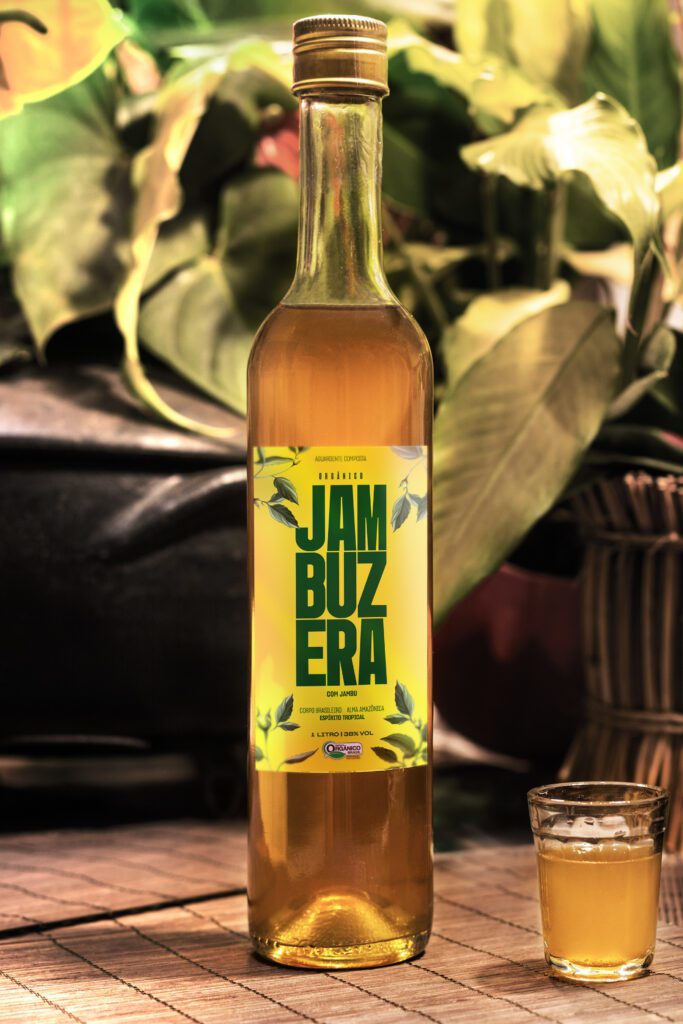 Garrafa de vidro âmbar com tampa preta da Jambuzera, com rótulo branco ilustrado com folhas tropicais verdes. O logotipo da marca aparece em destaque no centro, transmitindo um estilo artesanal e natural.